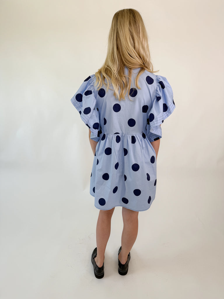 Light blue mini dress with navy polka dots, collared neckline, button-down front, and flutter sleeves.