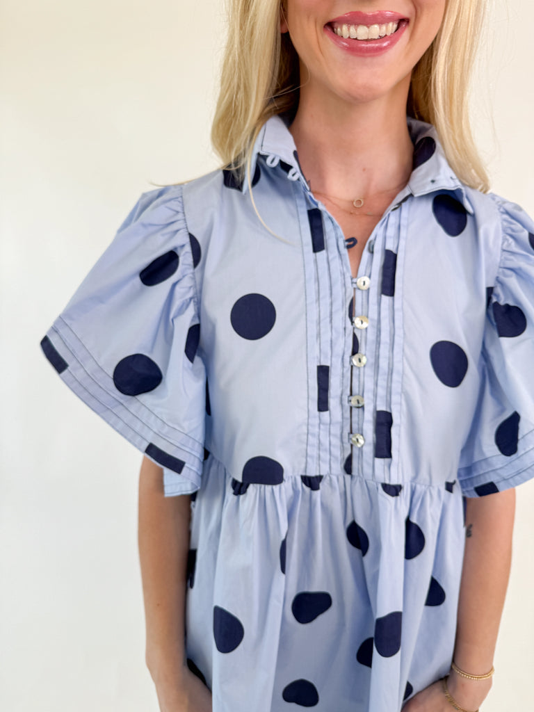 Light blue mini dress with navy polka dots, collared neckline, button-down front, and flutter sleeves.