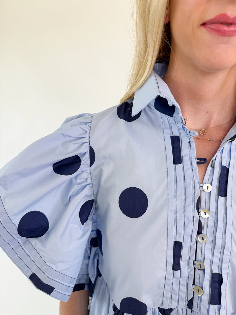 Light blue mini dress with navy polka dots, collared neckline, button-down front, and flutter sleeves.