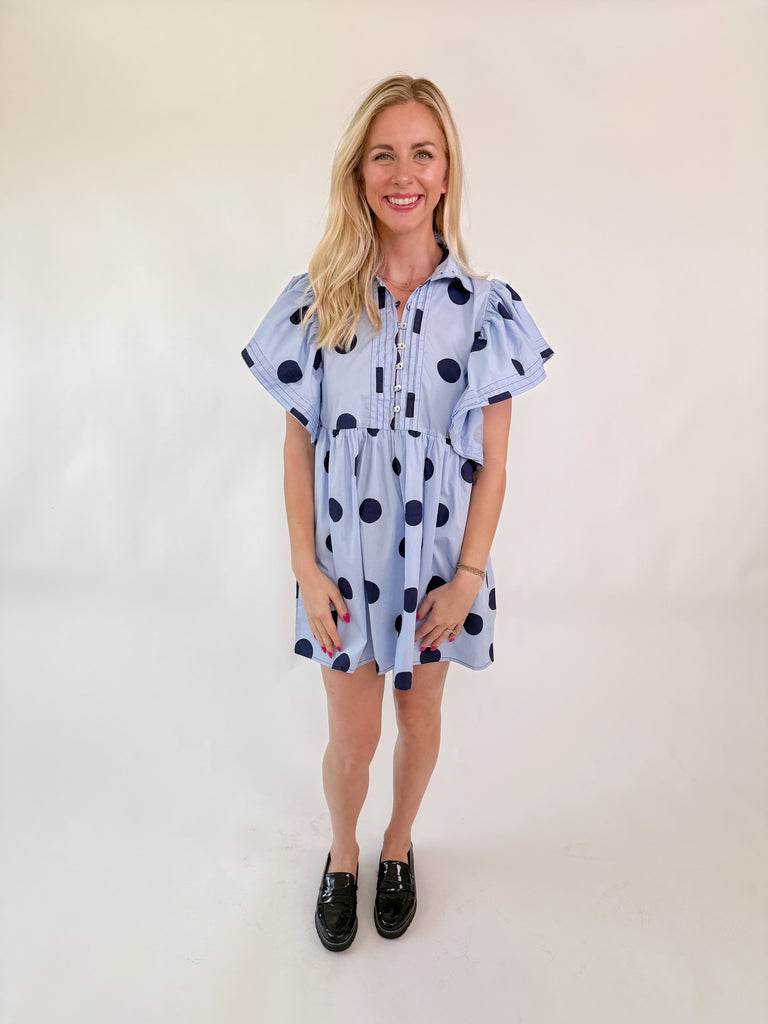 Light blue mini dress with navy polka dots, collared neckline, button-down front, and flutter sleeves