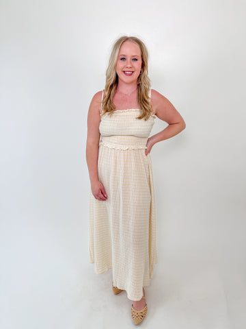 Woman wearing a cream-colored maxi dress with smocked top, double straps, and ruffle trim