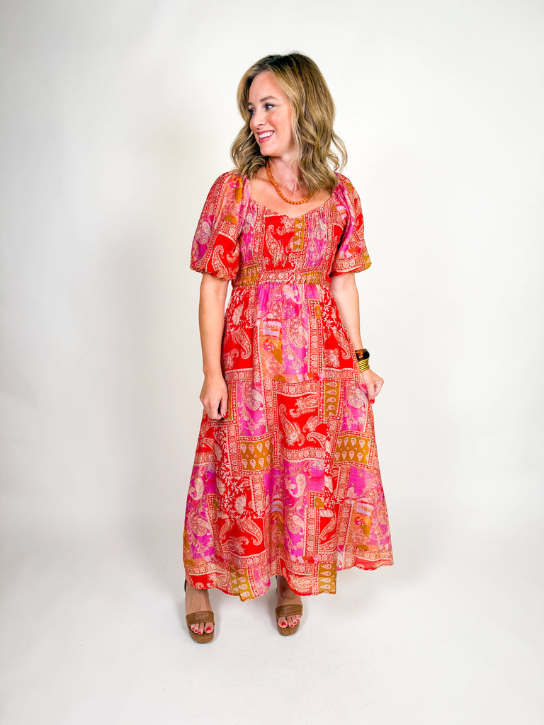 Woman wearing a red and pink bohemian-inspired maxi dress with puff sleeves, square neckline, and flowing skirt