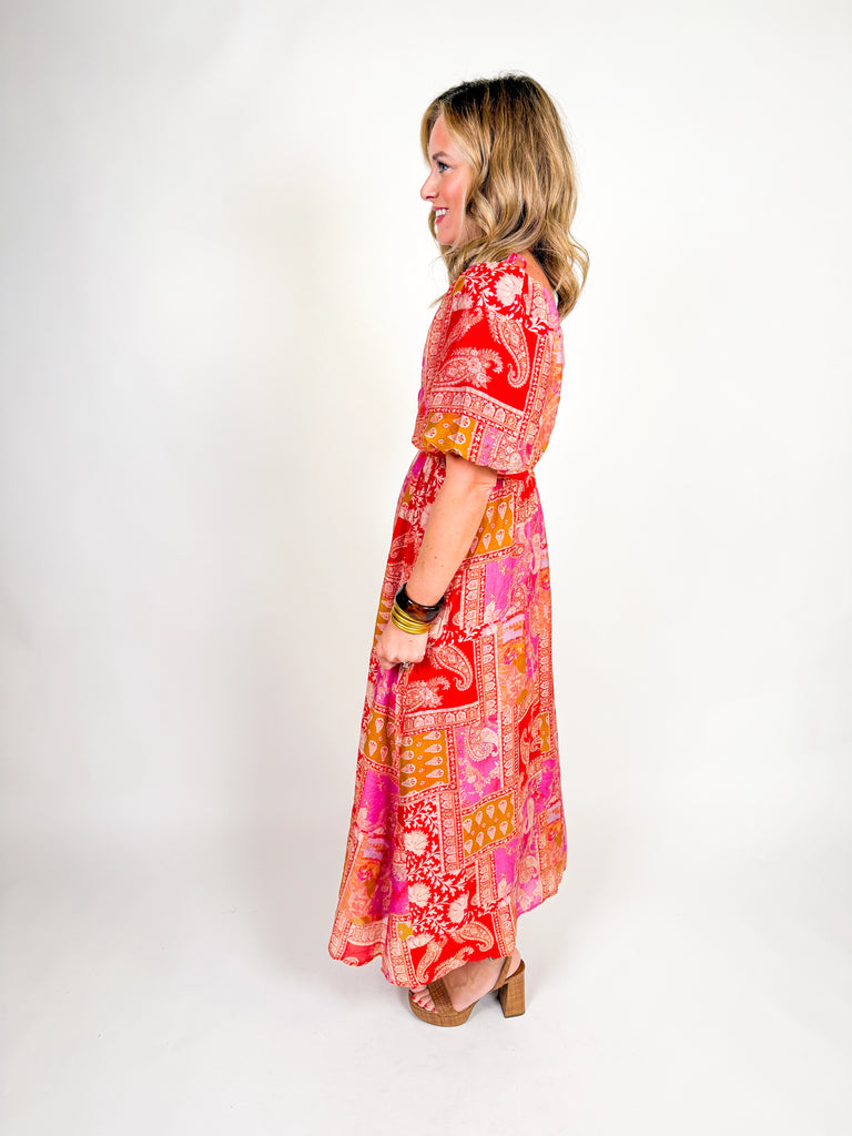Woman wearing a red and pink bohemian-inspired maxi dress with puff sleeves, square neckline, and flowing skirt