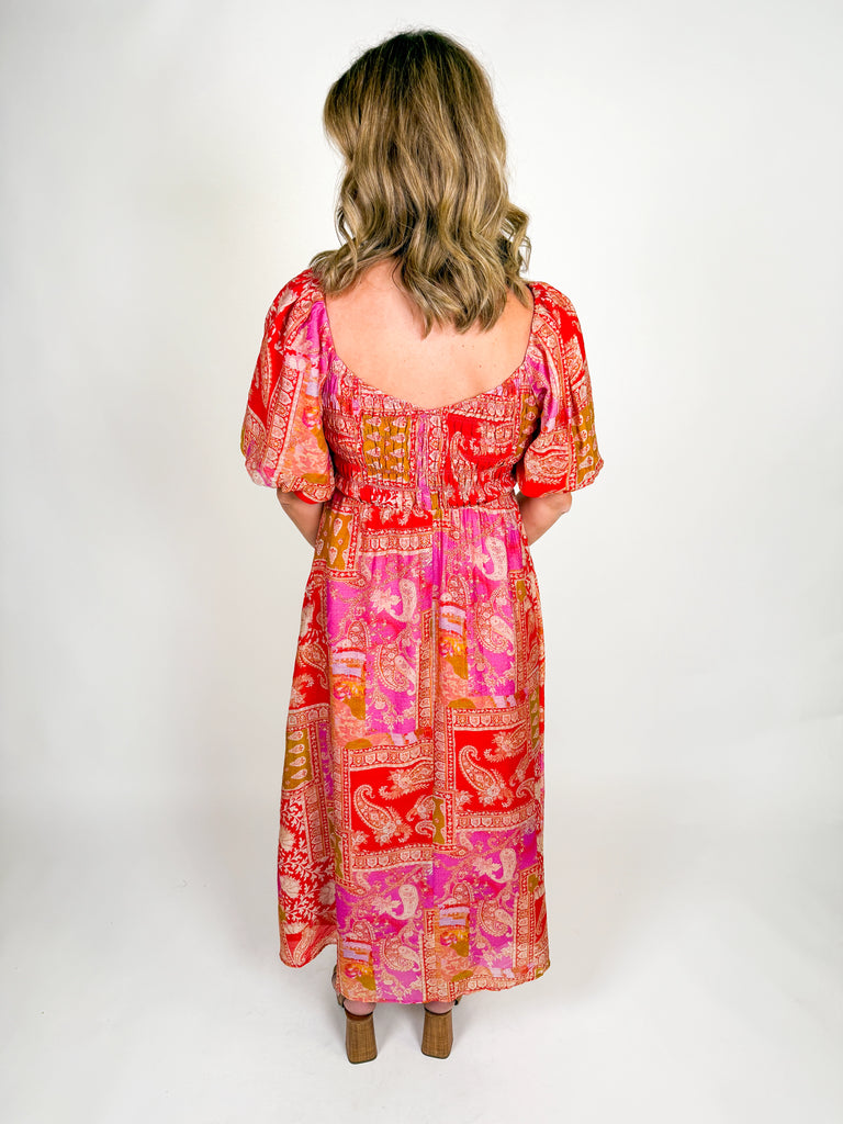 Woman wearing a red and pink bohemian-inspired maxi dress with puff sleeves, square neckline, and flowing skirt