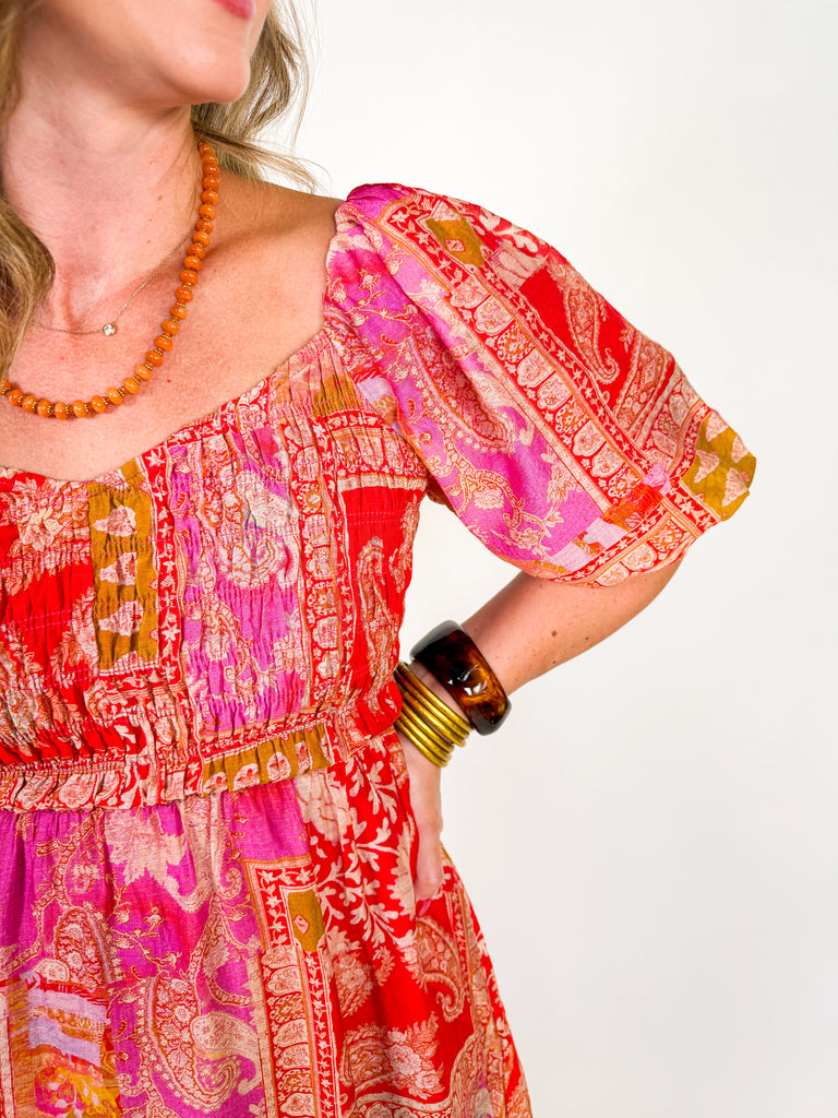 Woman wearing a red and pink bohemian-inspired maxi dress with puff sleeves, square neckline, and flowing skirt