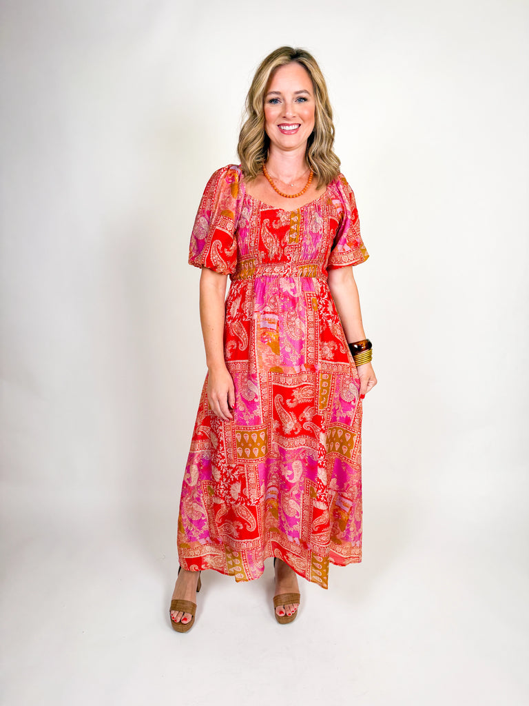 Woman wearing a red and pink bohemian-inspired maxi dress with puff sleeves, square neckline, and flowing skirt