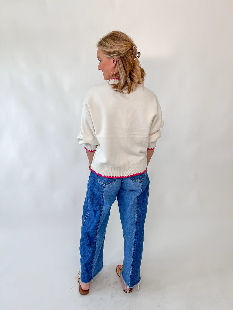 Woman wearing cream cardigan with fruit embroidery and pink trim