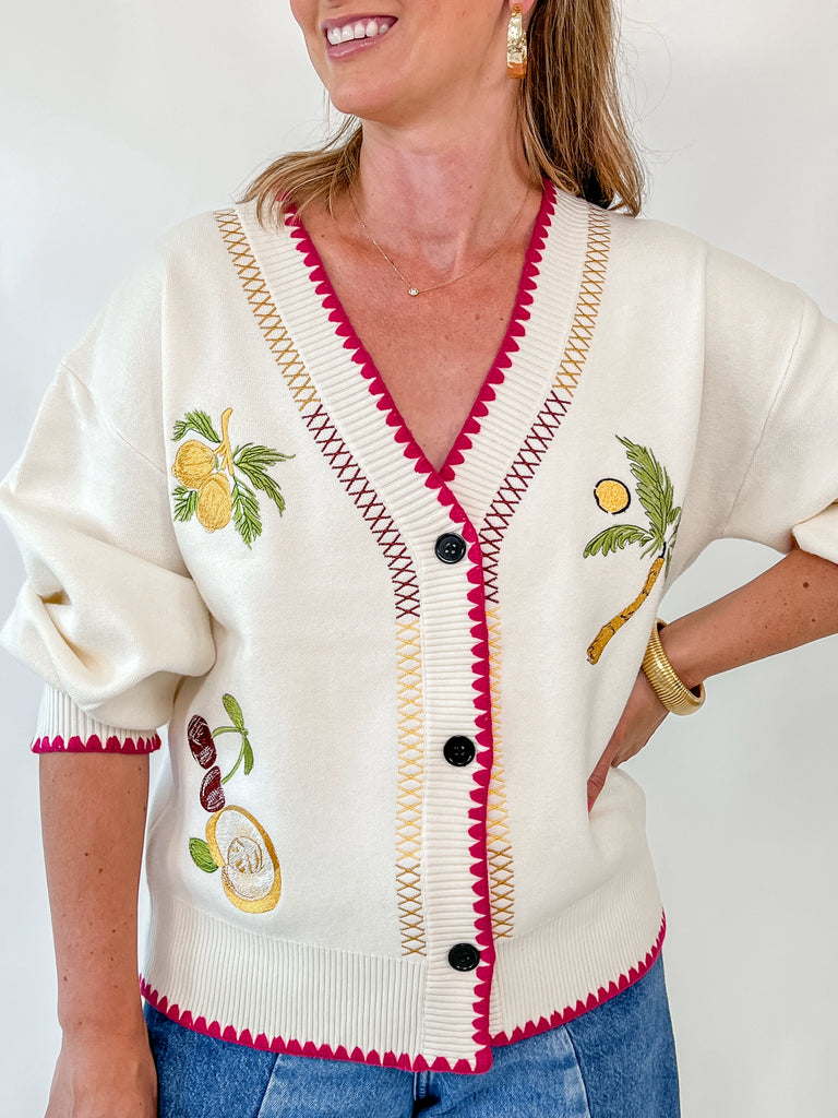 Woman wearing cream cardigan with fruit embroidery and pink trim