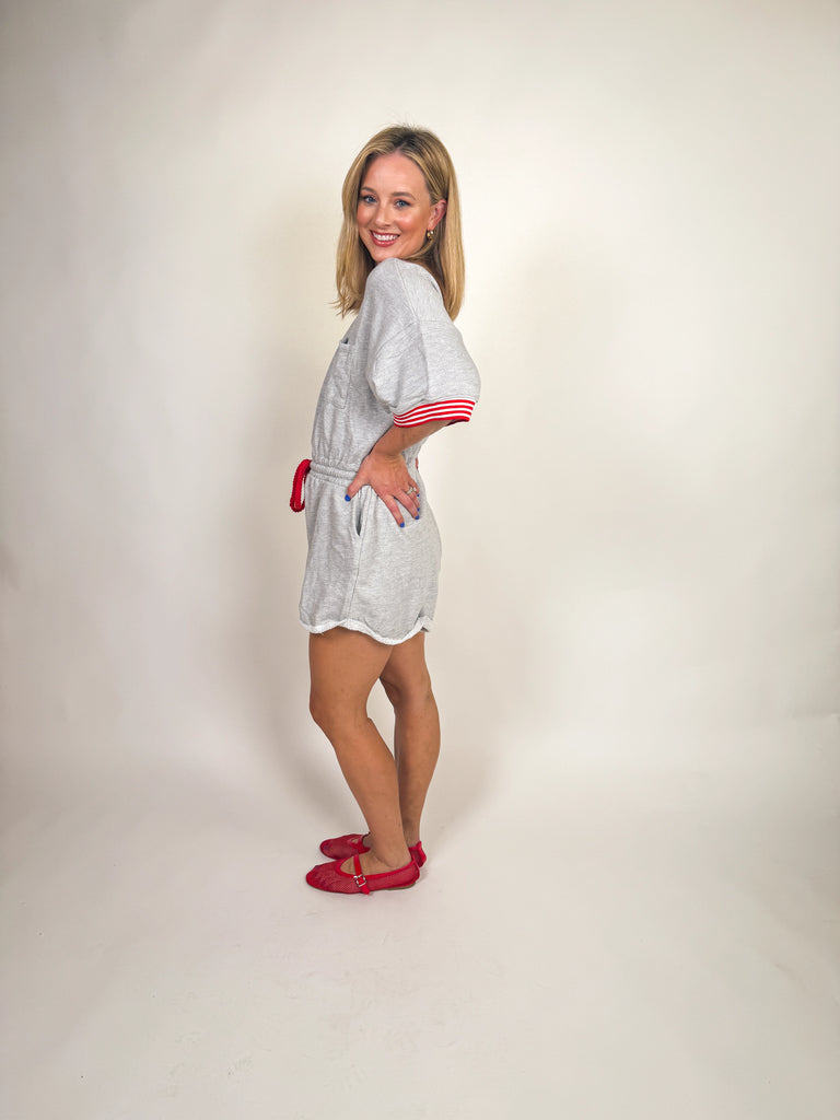 Woman wearing a heather gray romper with red striped trim and drawstring tie