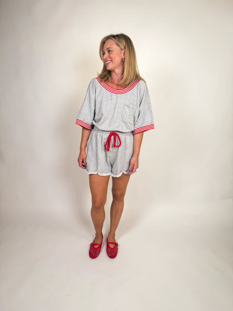 Woman wearing a heather gray romper with red striped trim and drawstring tie