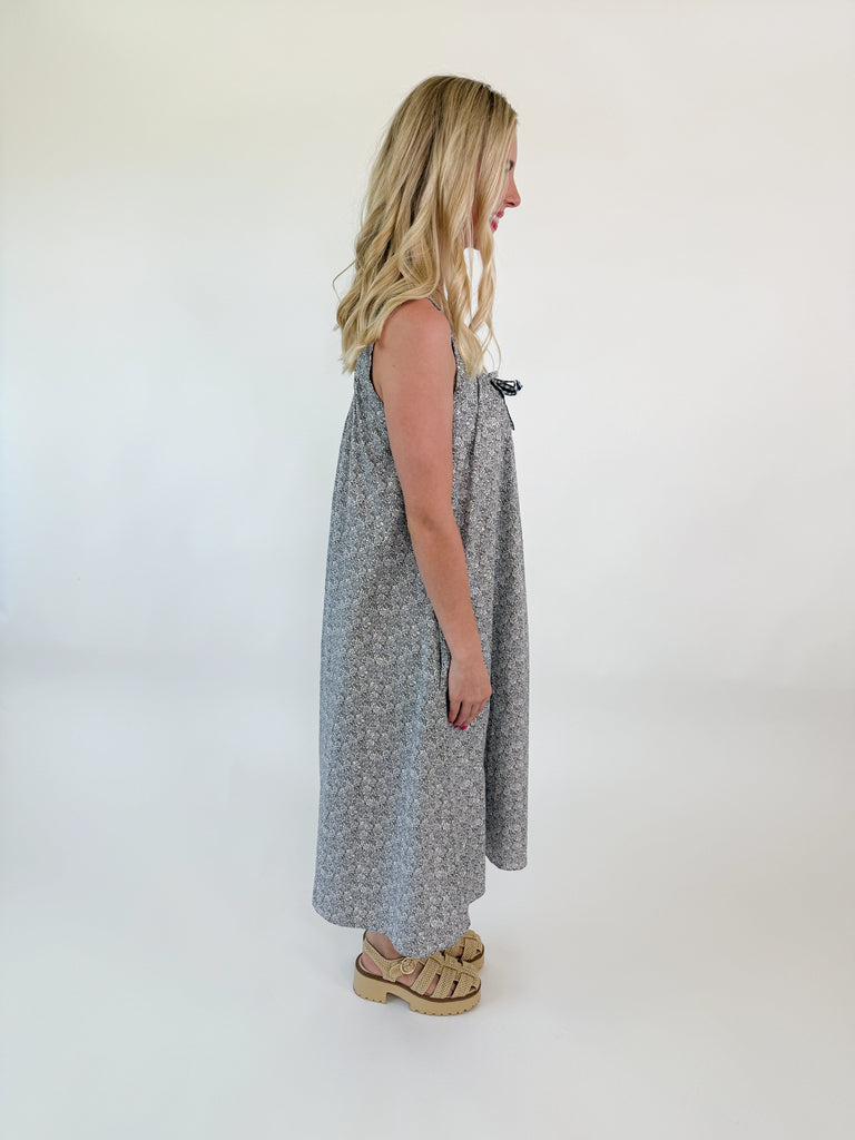 Girl wearing a grey floral midi with tie neckline, wide straps, and side pockets