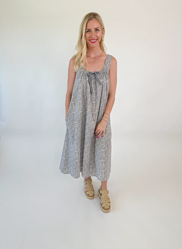 Girl wearing a grey floral midi with tie neckline, wide straps, and side pockets